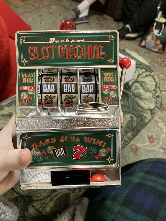 Toy slot machine with jackpot symbols, held by a person in a festive setting.