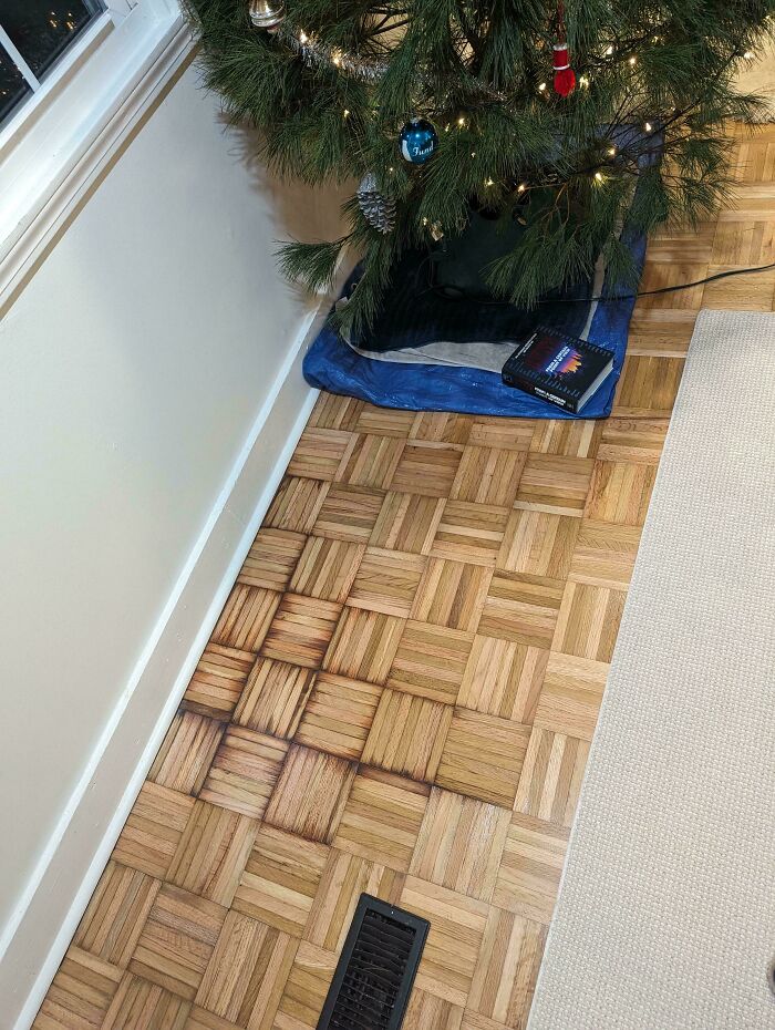 Christmas tree accident with heat damage on wooden floor; vent causing discoloration.