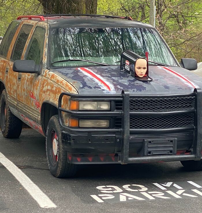 Rusty SUV with doll head on hood, exemplifying car-fails humorously parked.