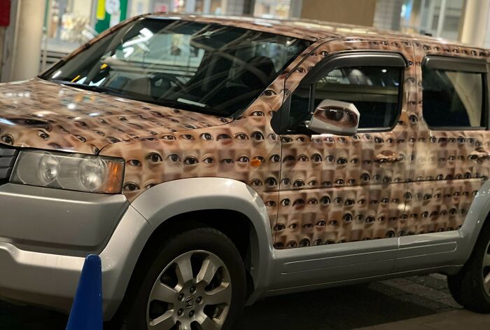 Car covered in eye-themed wrap, showcasing a unique design in a parking garage. Car-Fails.