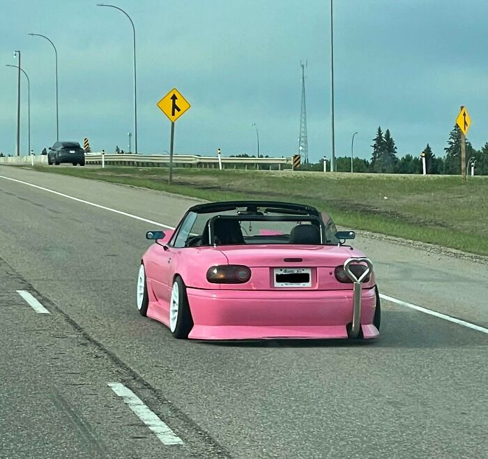 Pink convertible with heart-shaped exhaust driving on highway, showcasing interesting things on the road.