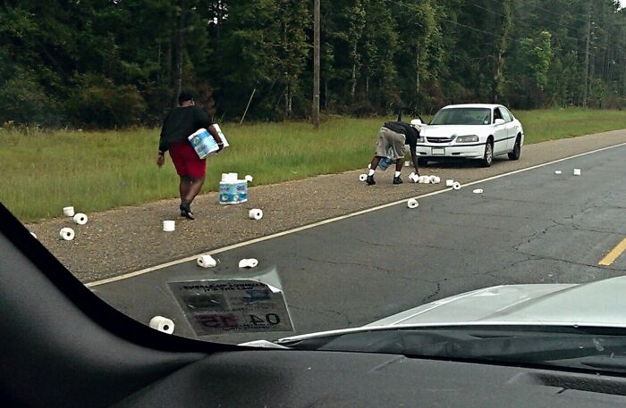 People picking up scattered toilet paper on the roadside near a parked car, highlighting interesting things on the road.