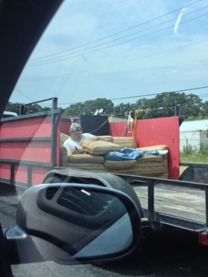 Person relaxing on a sofa in the back of a moving trailer, captured on the road.