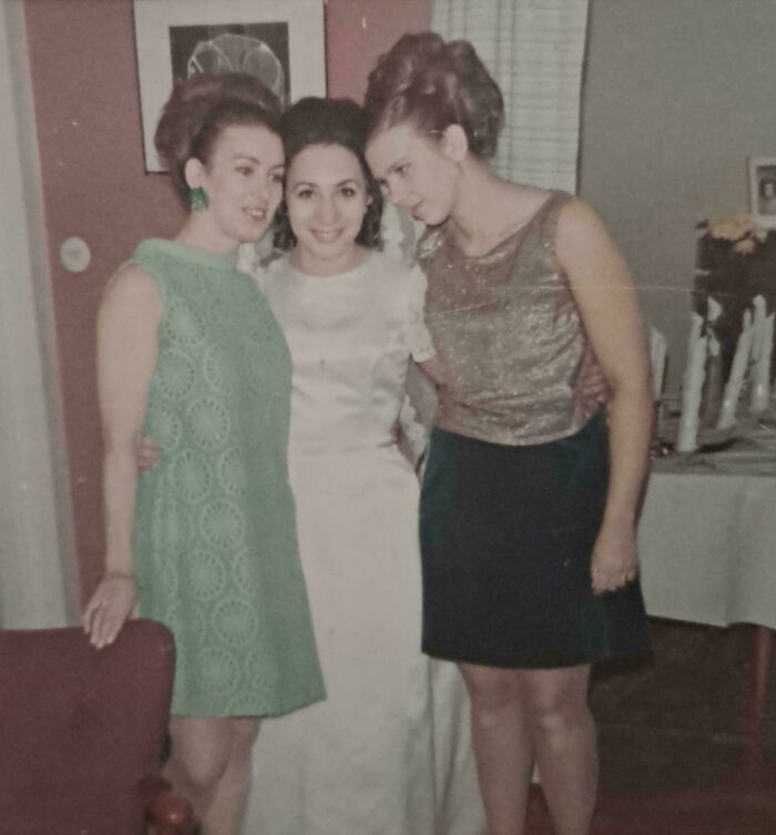 Three women in 60s fashion, wearing a green dress, a white gown, and a gold top with black skirt, posing together indoors.