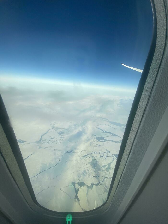 View of ice formations through an airplane window under a vivid blue sky; a fascinating aerial perspective.