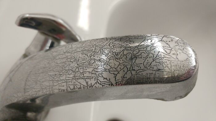 Scratched chrome faucet resembling a detailed map, showcasing fascinating patterns you have to see.