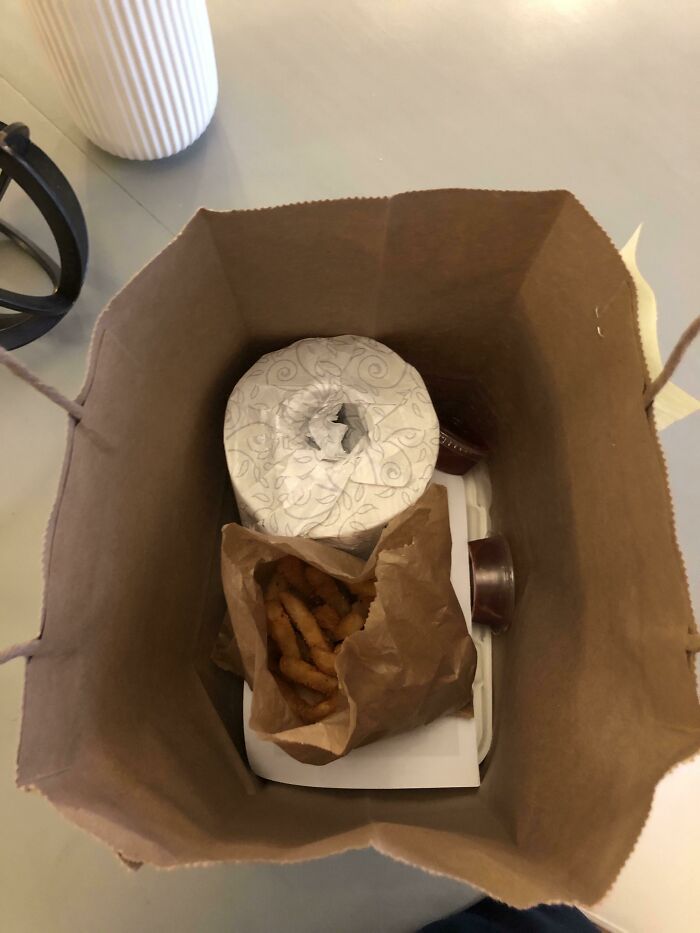 A paper bag containing curly fries, a roll of toilet paper, and a takeout box in an intriguing arrangement.