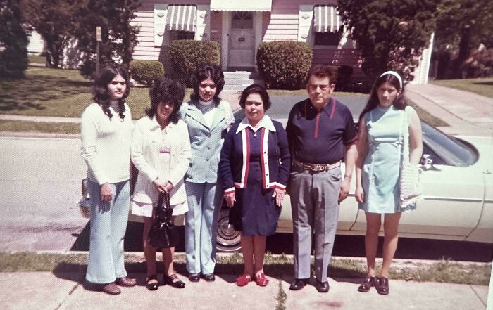 Family standing in front of a house, showcasing 60s fashion looks with colorful clothing and retro styles.