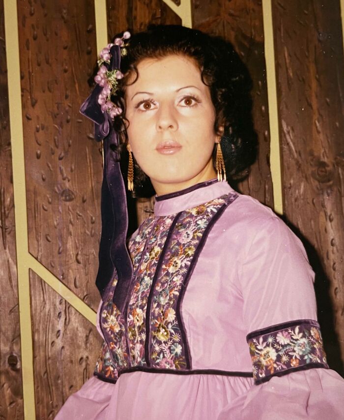 Woman in embroidered 60s fashion dress with floral details and purple accents against a wooden backdrop.