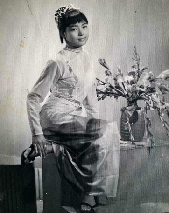 Woman wearing a stylish 60s fashion ensemble, seated beside a vase of flowers, exuding vintage elegance.