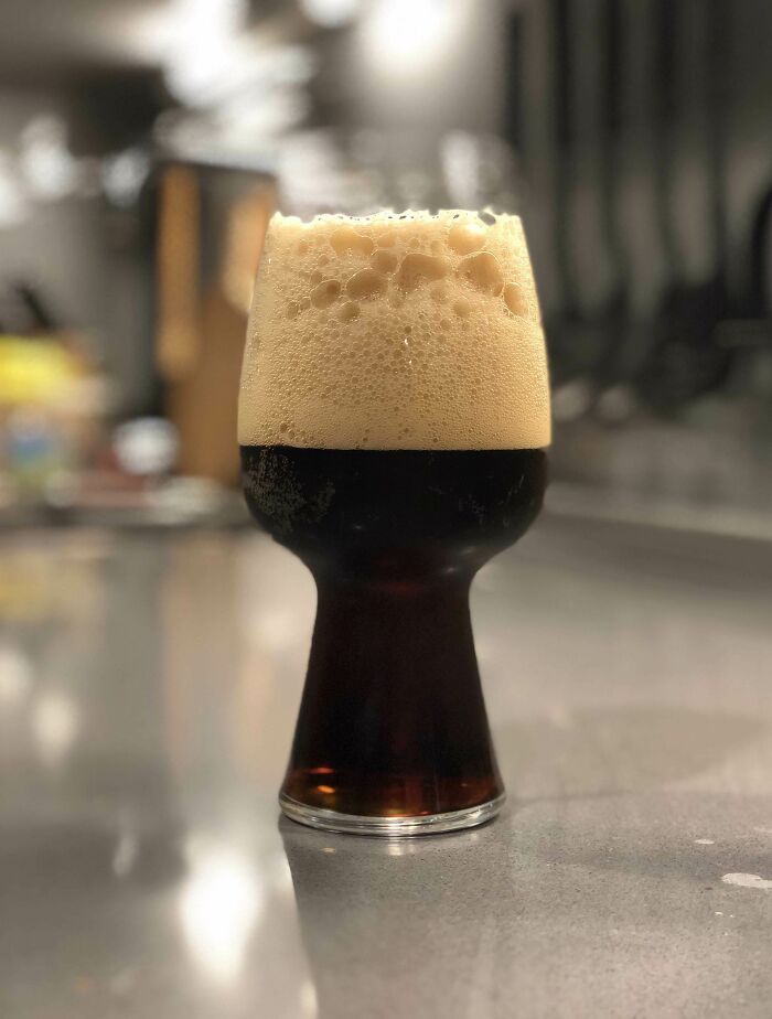 Glass of dark beer with frothy head in a modern kitchen, highlighting fascinating beverage presentation.