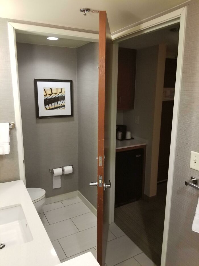 Bathroom with unusual door placement partially covering the toilet, creating a fascinating visual effect.