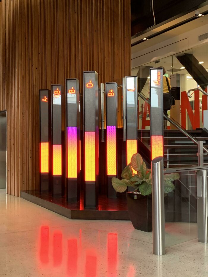 Colorful light pillars in a modern lobby with a staircase and plants, creating a fascinating visual effect.