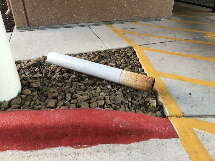 Large cigarette sculpture on pavement, resting among small rocks, highlighting optical illusion.