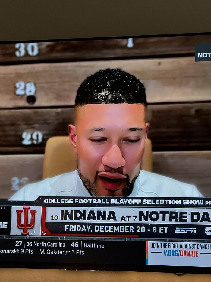 Man with a hairstyle accident shown on TV during a college football show.