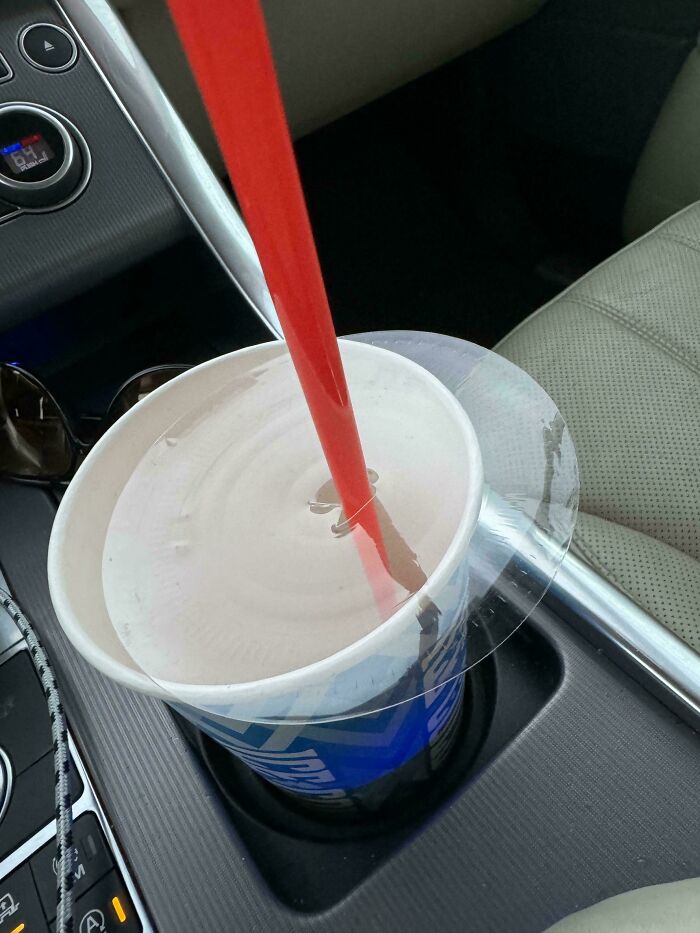 Unusual image of a red straw piercing an intact plastic lid of a cup in a car's cup holder.