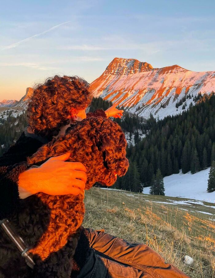 A person with a dog, pointing at a snowy mountain at sunset, creating a fascinating scene.