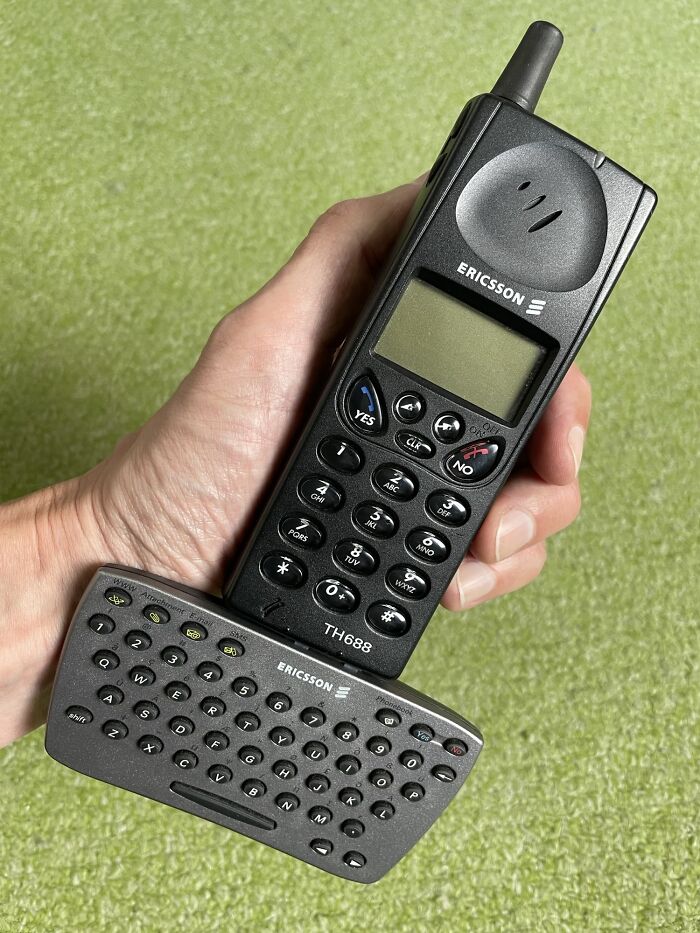 Vintage Ericsson phone with attached keyboard, held in hand against a green background.