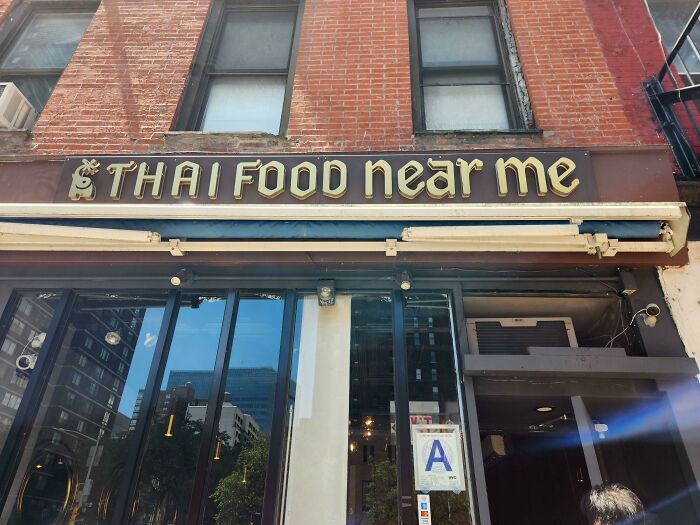 Thai restaurant sign on brick building, reading "Thai Food Near Me," under a clear sky.