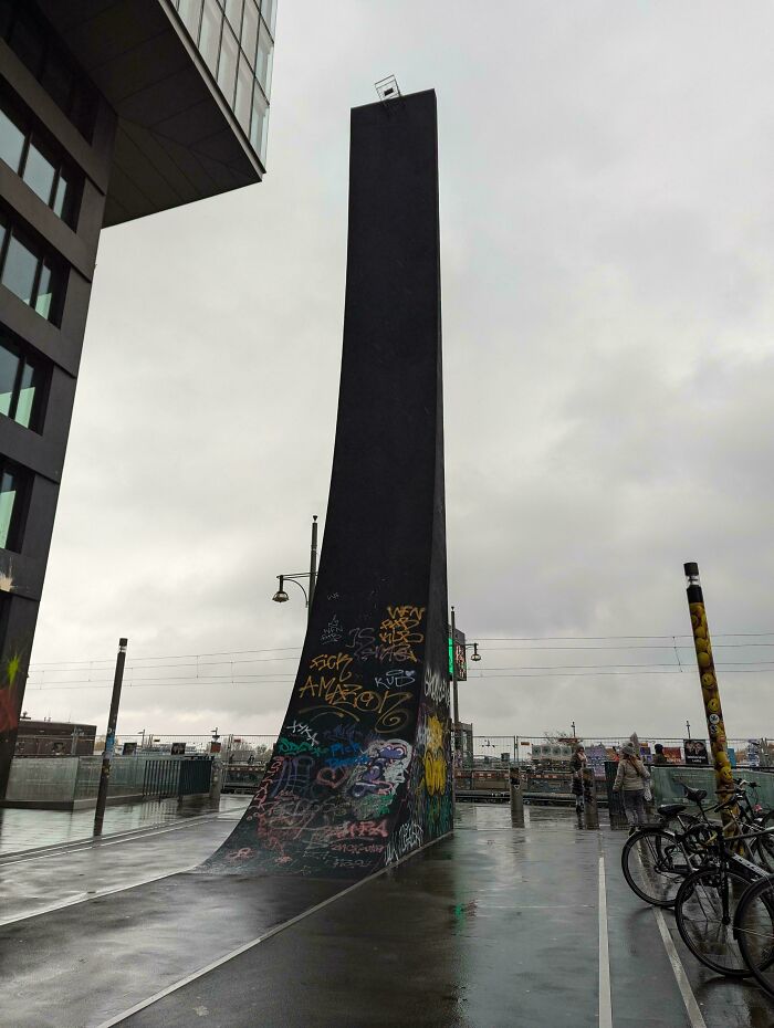 Graffiti-covered, towering black structure against a cloudy sky, showcasing a fascinating urban scene.