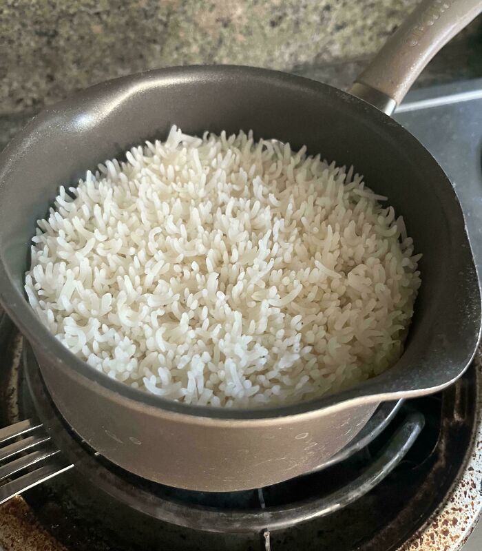 A pot of cooked white rice on a stove, showcasing fascinating texture and color contrast.