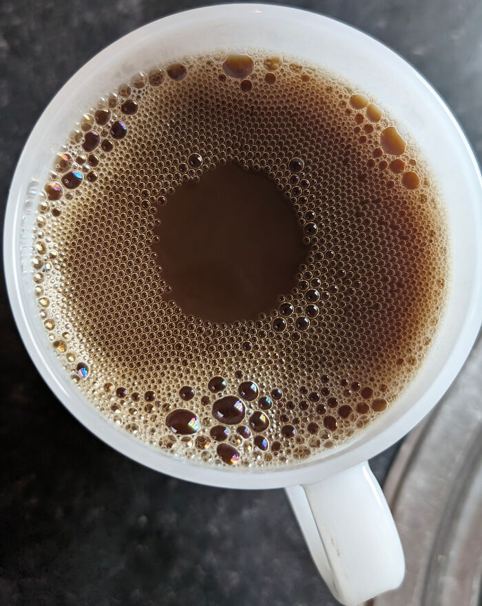 Aerial view of a coffee cup with bubbles on a dark surface, showcasing fascinating visual textures.