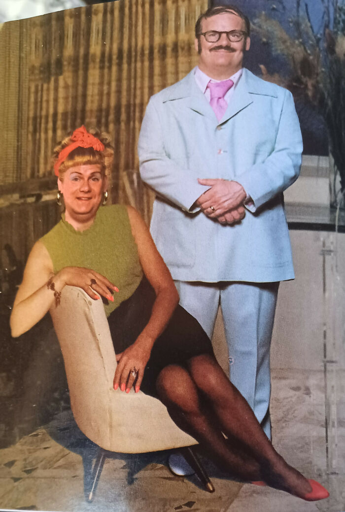 Man in light blue suit and woman in 60s fashion with a green top and orange headband, posing in a classic setting.