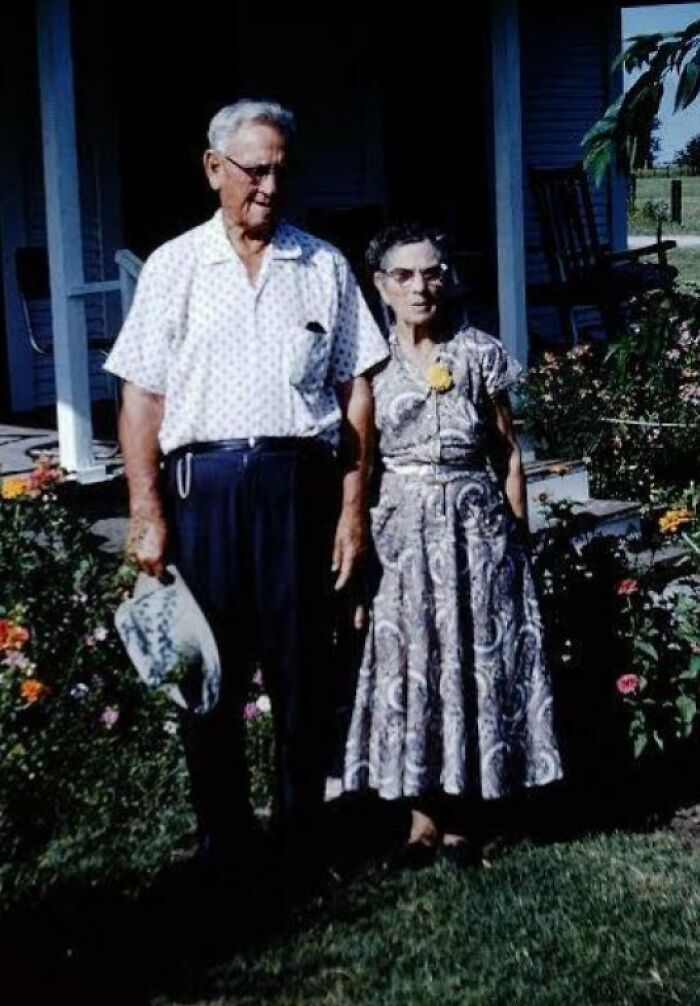 Elderly couple in 60s fashion standing in garden, woman in a patterned dress, man in a polka dot shirt.