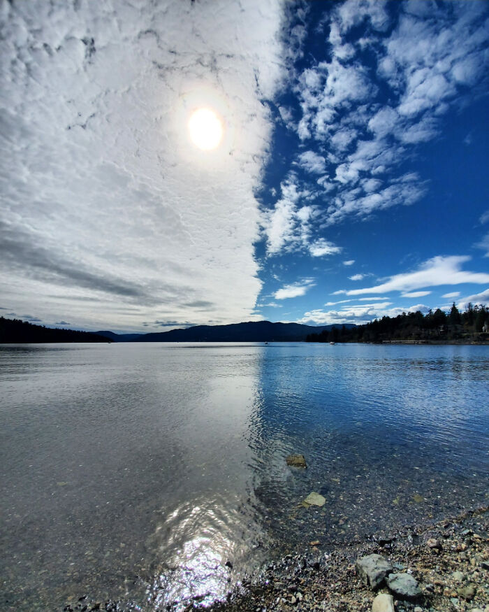 Fascinating pic of a lake under a dramatic sky split between clouds and clear blue, with sunlight reflecting on the water.