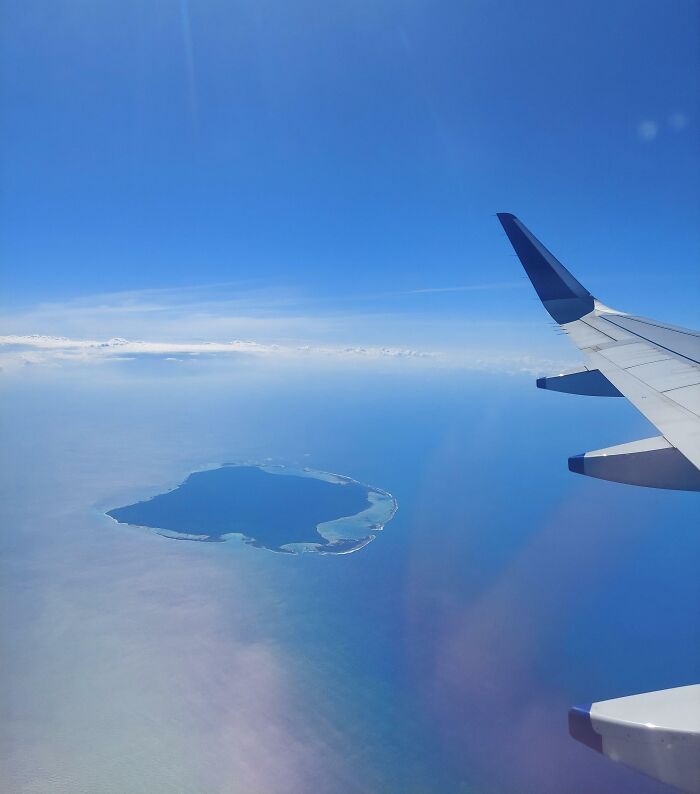 Airplane wing over stunning blue ocean with a lone island, capturing a fascinating aerial view.