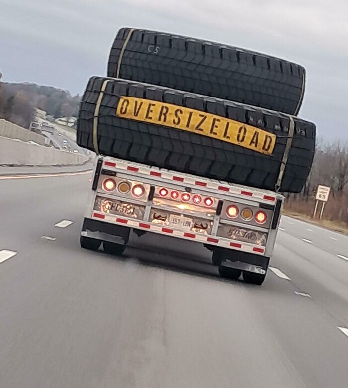 Truck carrying oversized tires on the highway marked "Oversize Load", fascinating transport scene.