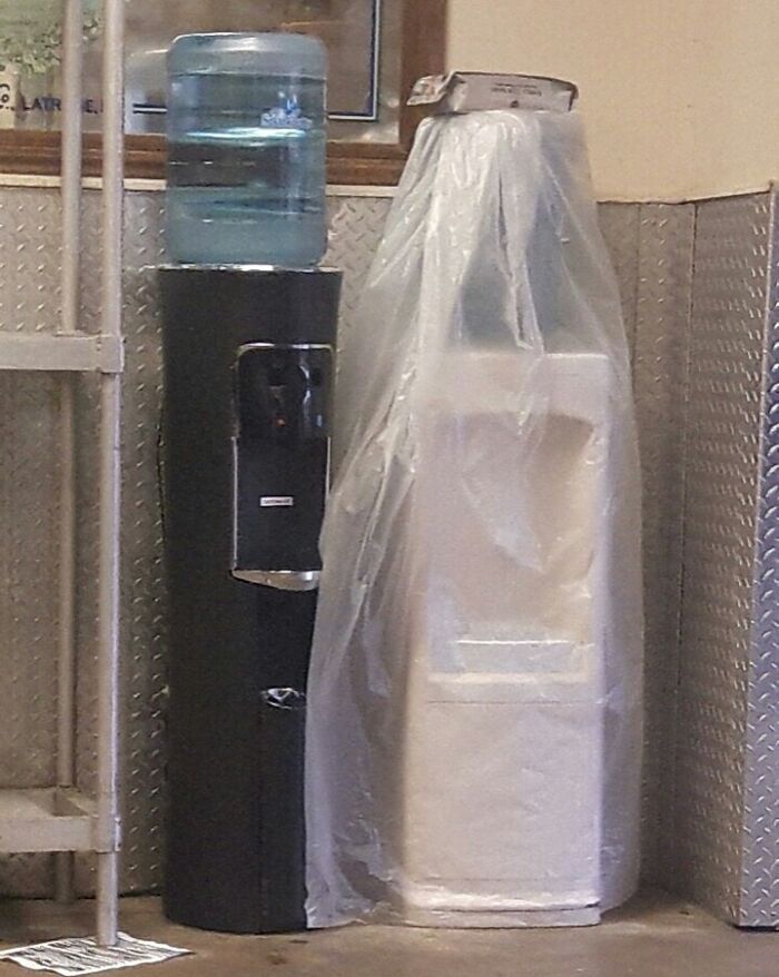 Water coolers in a break room, one unwrapped and one still wrapped in plastic. Fascinating pic highlighting everyday objects.