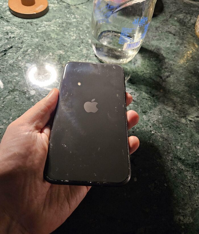 A mesmerizing reflection of a light bulb on an iPhone screen held over a green marble surface.