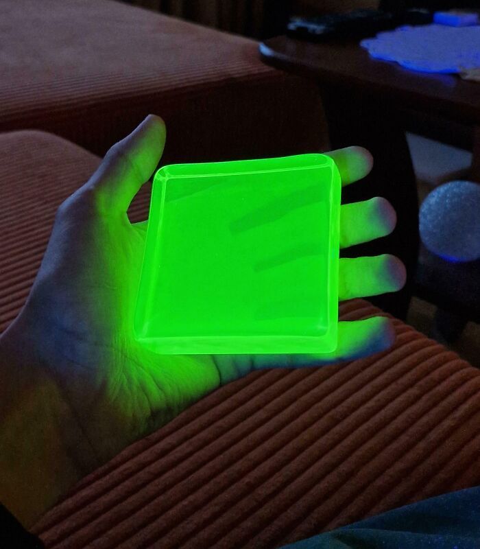 A hand holding a glowing green square object in a dimly lit room.