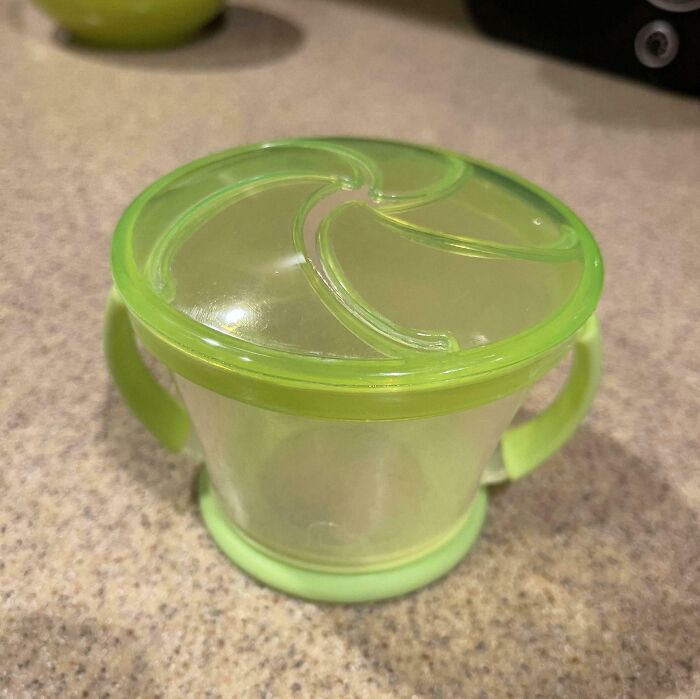 Green toddler snack cup with lid on a counter, showcasing a parenting genius trick for mess-free snacking.