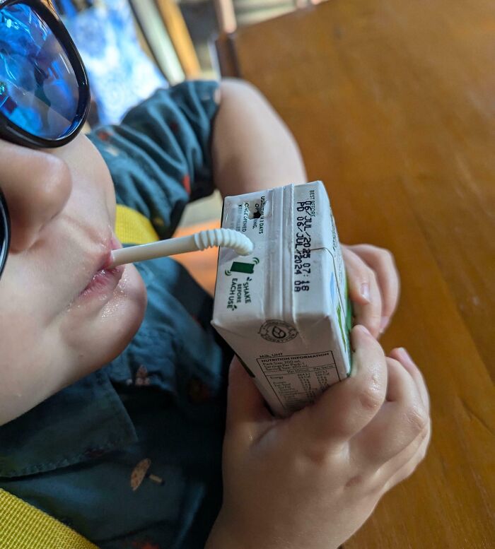 Child wearing sunglasses drinks from a clever juice box hack, showcasing parenting genius tricks.