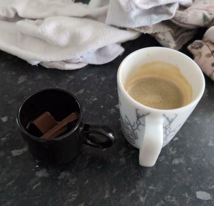 Coffee cup and chocolate in black mug on counter with laundry; a parenting genius trick setup.