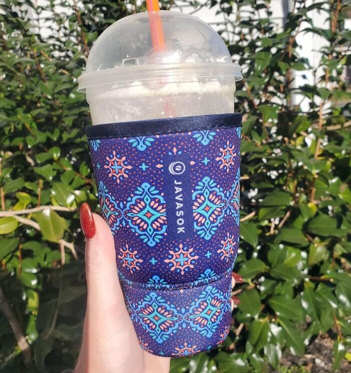 Hand holding a drink in a colorful cup sleeve outdoors, showcasing a "brr basket" moment.