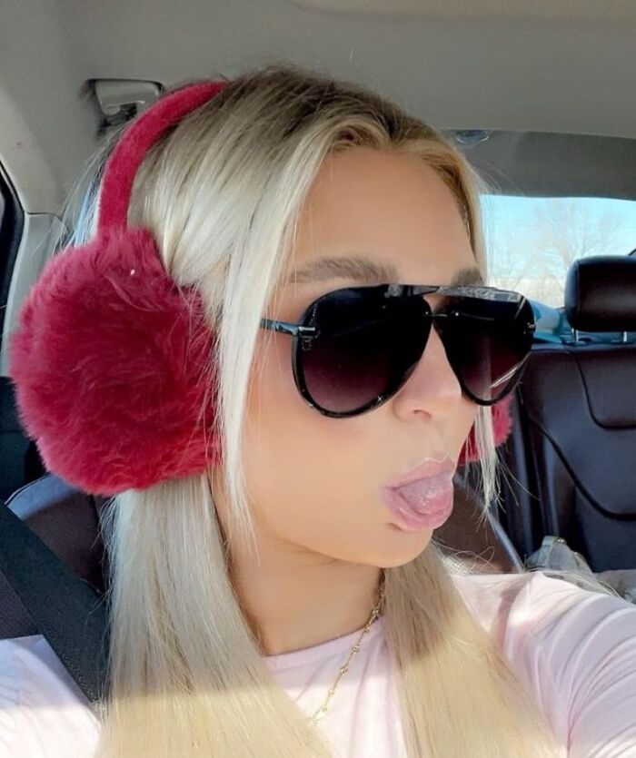 Woman wearing sunglasses and red earmuffs, sitting in a car.