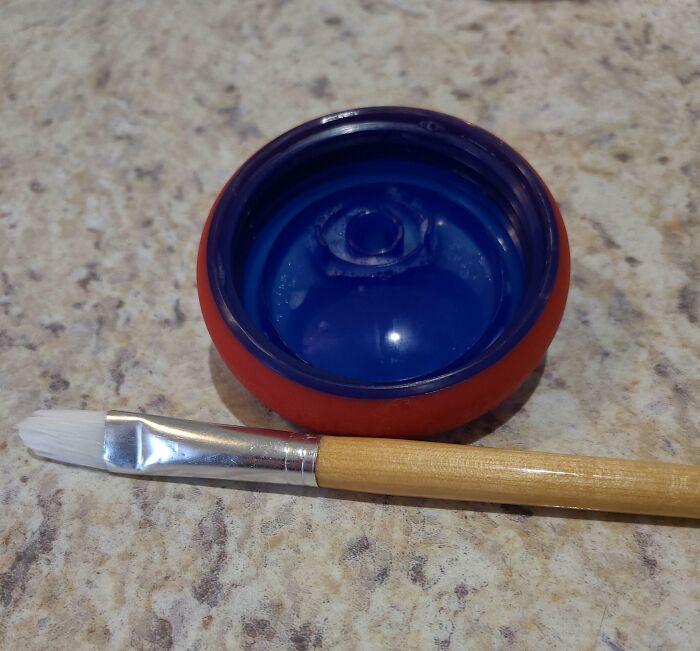 Plastic lid with blue paint inside, next to a small paintbrush on a countertop, showing a parenting-genius-trick.