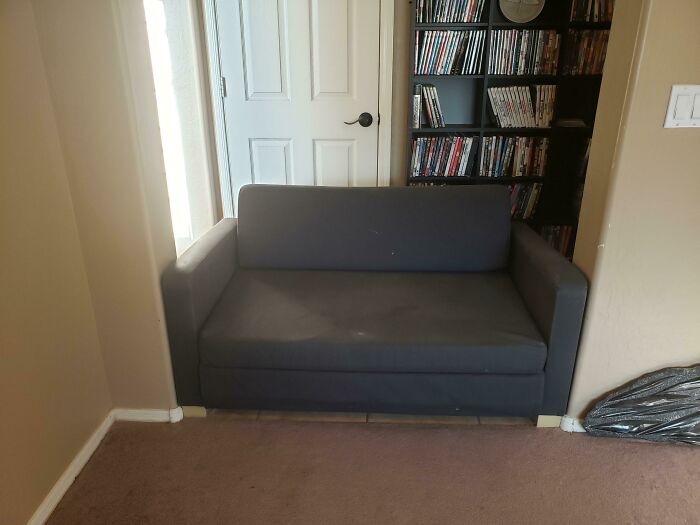 Gray couch perfectly fitting in a nook, showcasing satisfying-perfect-fit in a room with DVDs and a door nearby.