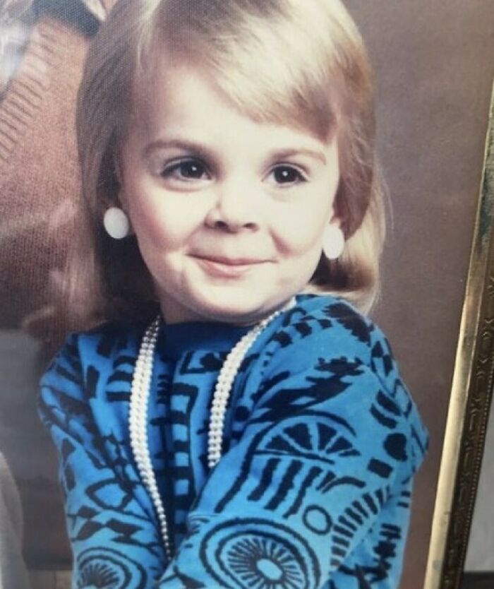 Child in vintage attire and pearl necklace, posing for a family photo.