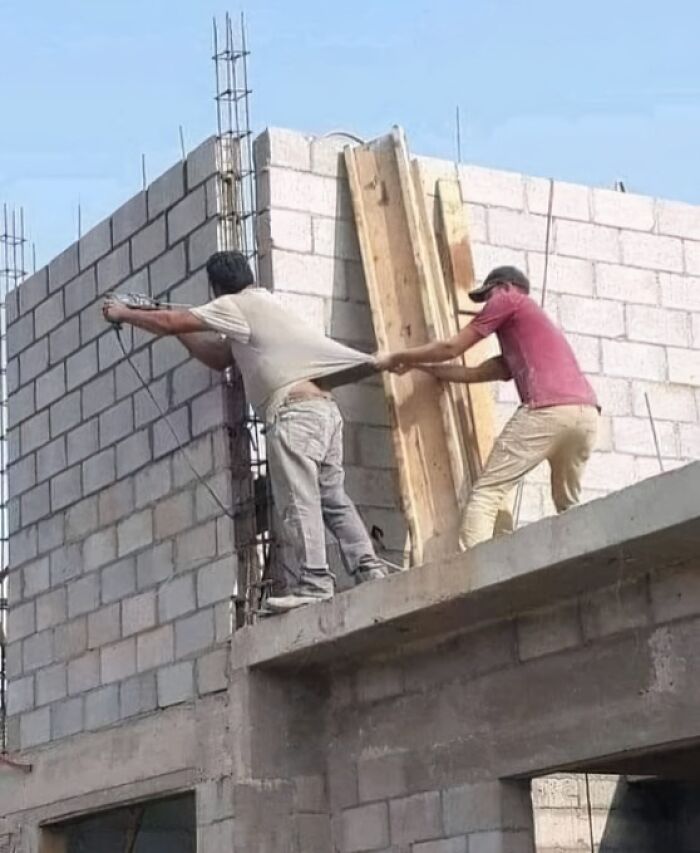 Two engineers on a construction site, one pulling the other's shirt, highlighting a humorous engineering mistake.