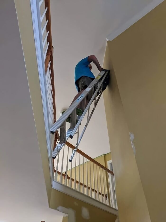 Engineer balancing precariously on a ladder between stair railings, showcasing questionable decision-making.