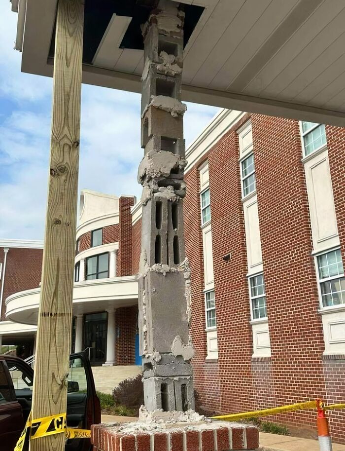 Cracked cinder block pillar with a brick exterior in front of a building, showcasing questionable engineering work.