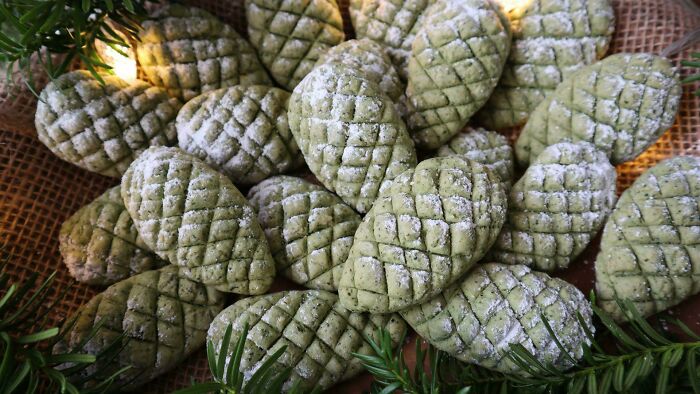 Festive pine cone-shaped cookies dusted with powdered sugar, surrounded by greenery for holiday snack inspiration.