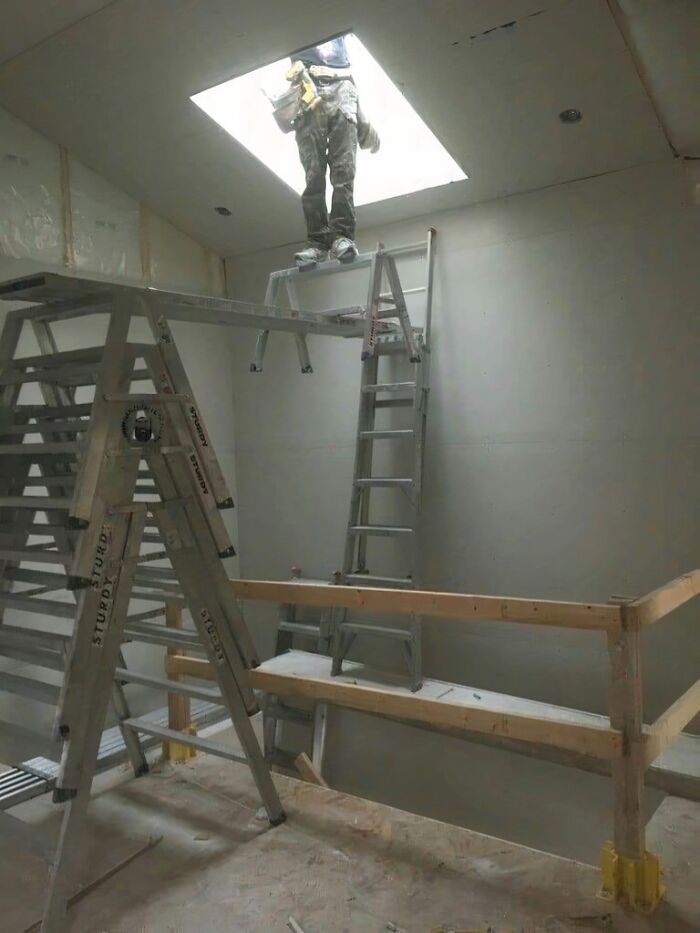 A person standing on a dangerously balanced ladder setup, illustrating a lack of smart engineering.