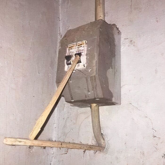 A makeshift wooden beam holds a circuit breaker switch, highlighting a questionable engineering solution.