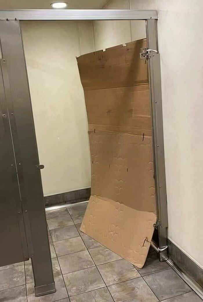 Improvised bathroom stall door made of cardboard, highlighting engineering mishap.