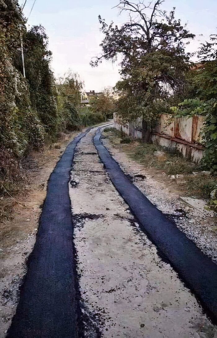 Poorly executed asphalt paving job on a narrow, tree-lined road, highlighting engineering mistakes.